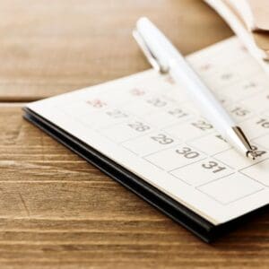 A calendar planner with a pen on a wooden table.