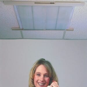 Smiling woman with curly hair indoors under a ceiling light.