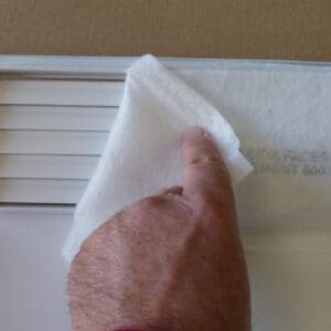 A finger lifting a corner of a white sticky note on a surface.