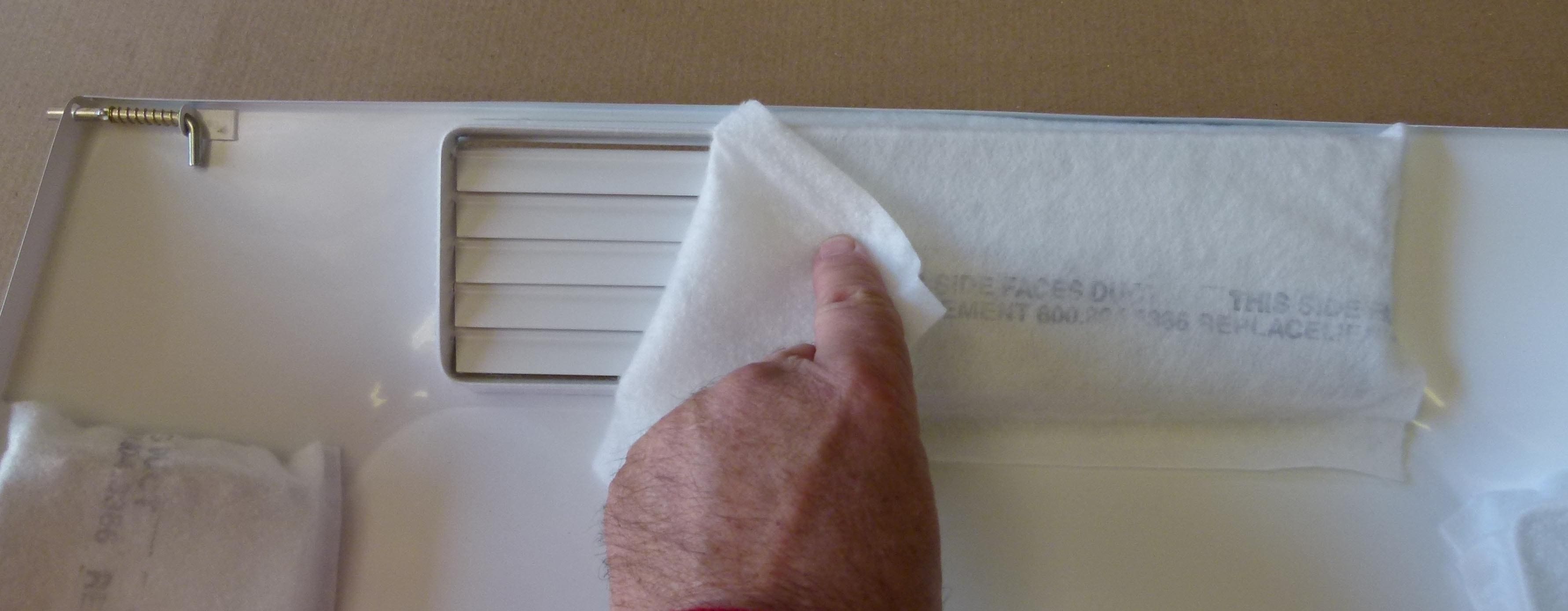 A finger lifting a corner of a white sticky note on a surface.