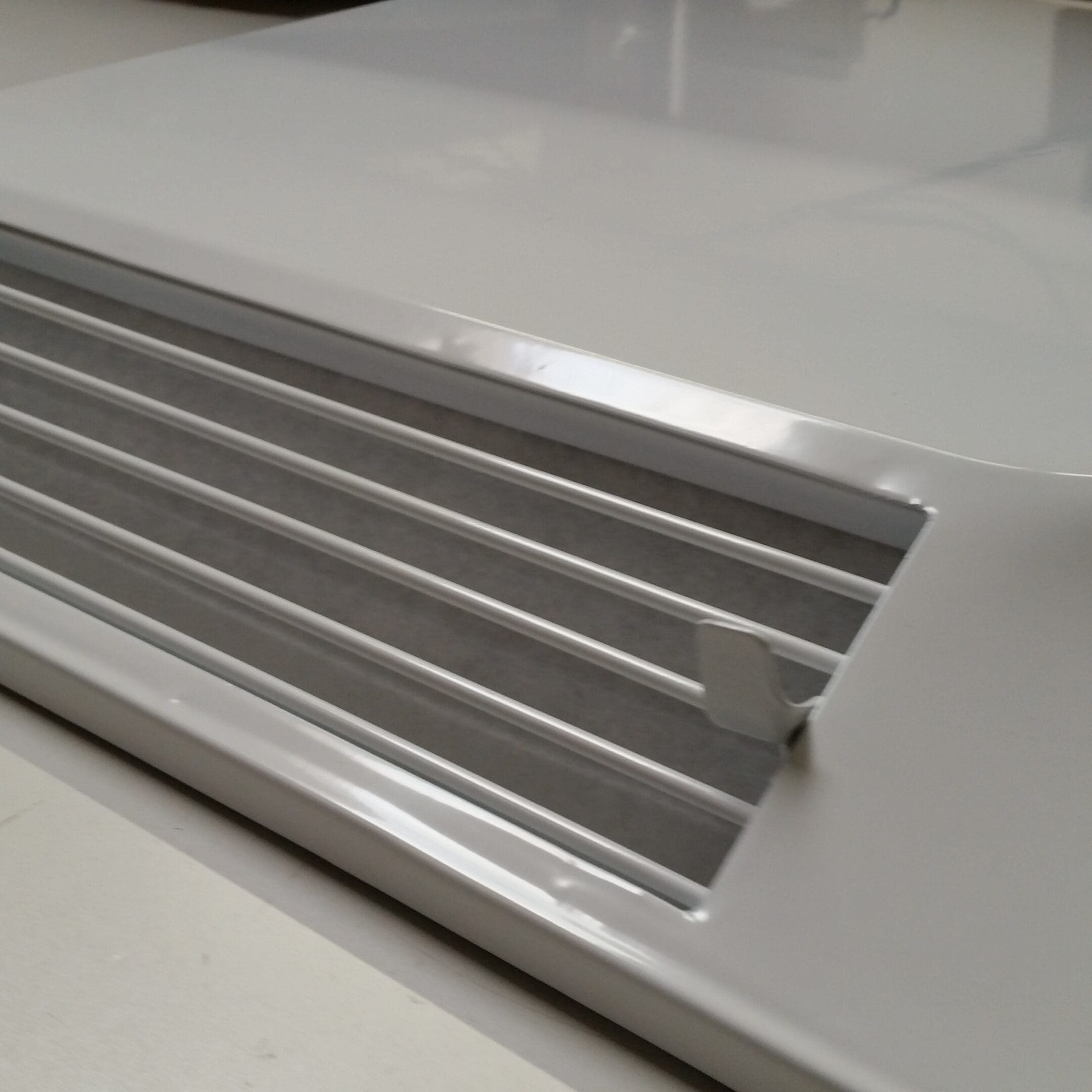 Close-up of a metallic linear vent on a white surface.
